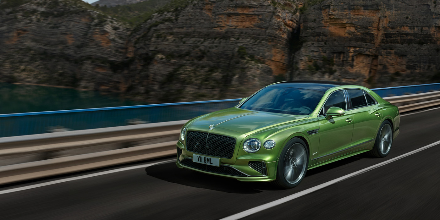 Bentley Belfast Bentley New Flying Spur Speed v8 hybrid sedan driving dynamically on a mountain road in Tourmaline Green paint