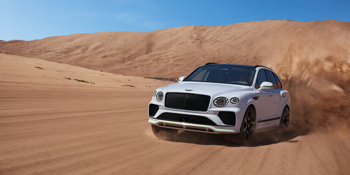 Bentley Belfast Bentley Bentayga Speed SUV front three quarter in Snow Quarts Pearlescent by Mulliner white paint driving dynamically through the desert