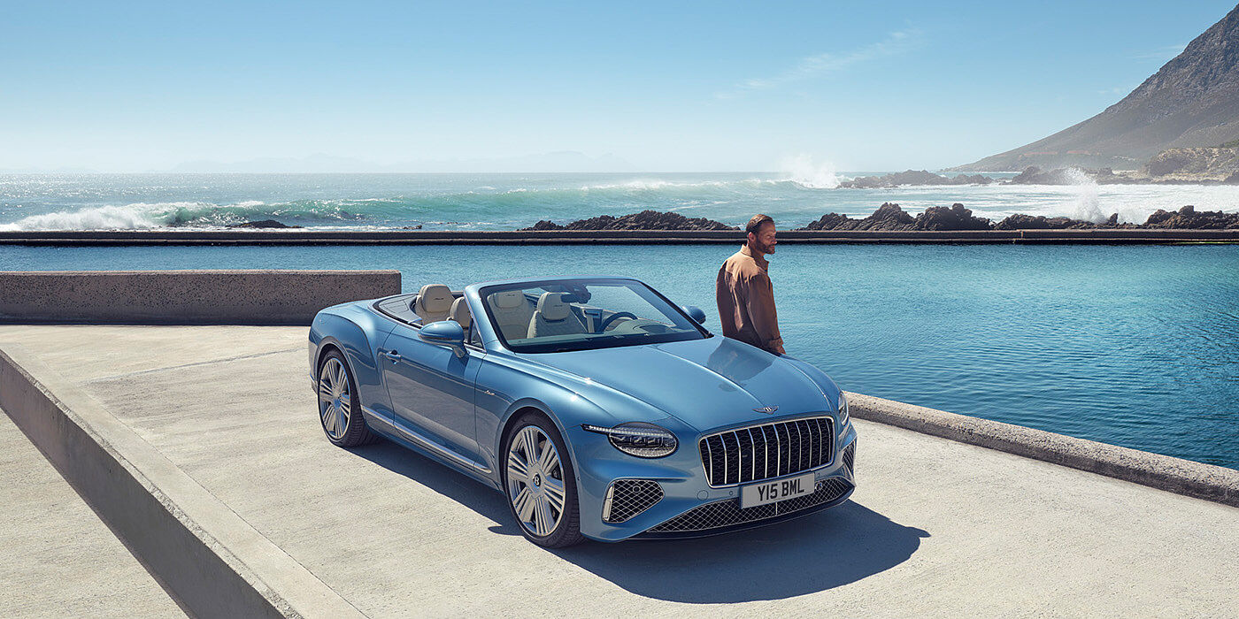 Bentley Belfast New Bentley Continental GTC Azure convertible front view in Light Windsor blue paint with 22 inch ten spoke wheels parked by the sea in the sunshine
