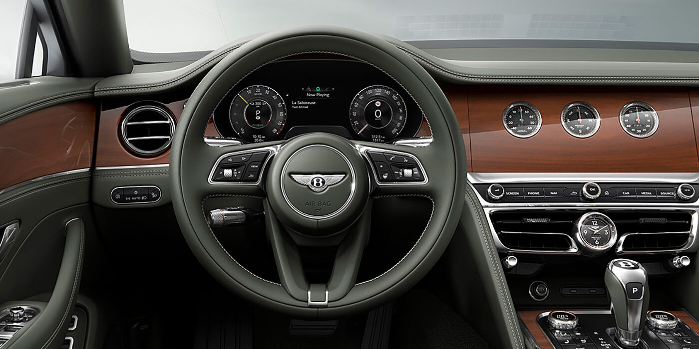 Bentley Belfast New Bentley Flying Spur sedan front cabin in Cumbrian Green hide and Crown Cut walnut veneer showing steering wheel and Rotating Display with three clocks on face