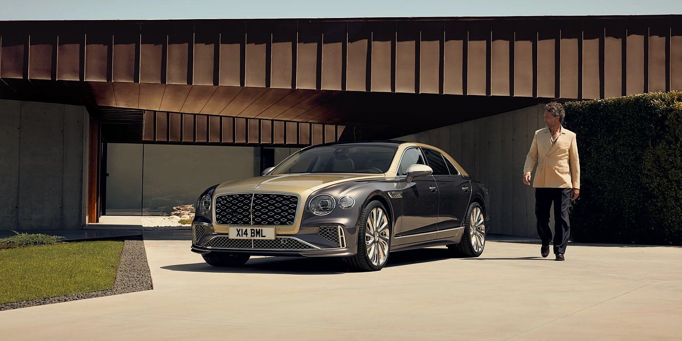 Bentley Belfast Bentley New Flying Spur Mulliner V8 hybrid sedan front three quarters in Rose Gold over Magnetic paint, parked near modern home