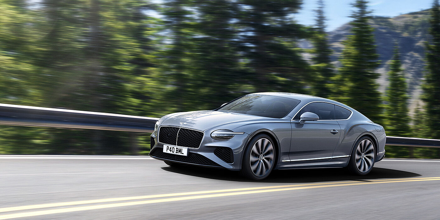 Bentley Belfast New Bentley Continental GT coupe in Silverlake paint and 22 inch ten-spoke wheels, driving dynamically on a tree-lined road in the sunshine