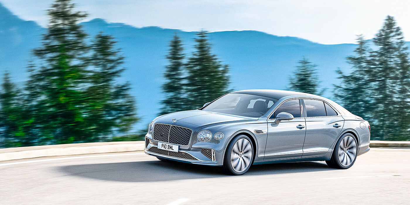 Bentley Belfast New Bentley Flying Spur sedan side view in Silverlake paint with ten spoke wheels and chrome matrix grille driving dynamically on a mountain road