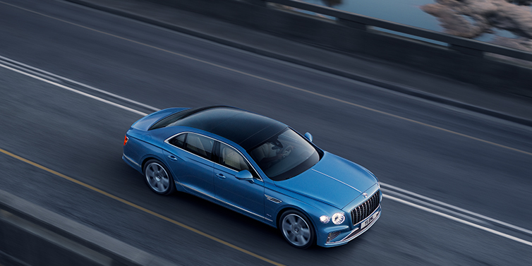 Bentley Belfast New Bentley Flying Spur Azure sedan in Light windsor blue paint by Mulliner, with 22 inch Azure wheels seen from overhead driving dynamically on a country road