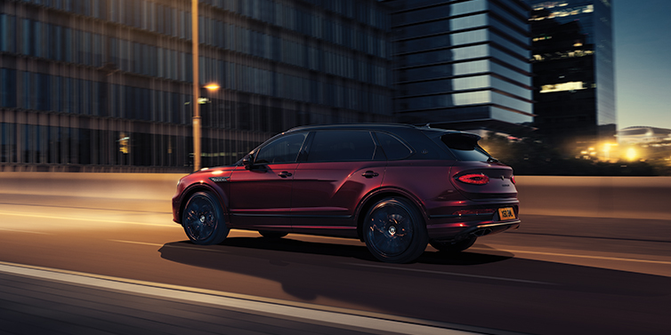 Bentley Belfast Bentley Bentayga Extended Wheelbase Mulliner SUV in Cricket Ball red paint driving dynamically in city at night